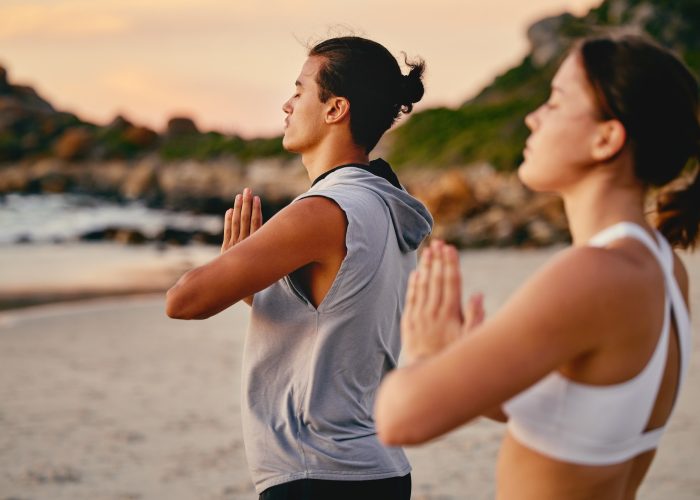 Couple, prayer hands and yoga meditation at beach outdoors for health and wellness. Sunset, pilates